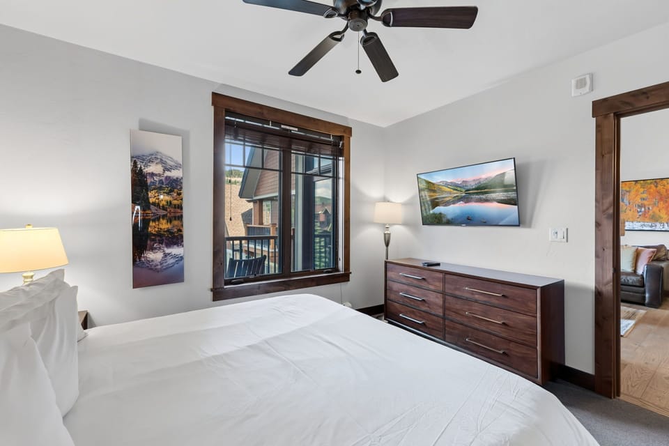 Your bright, peaceful bedroom features a plush bed under a ceiling fan, framed by mountain artwork and warm wood accents that invite total relaxation.