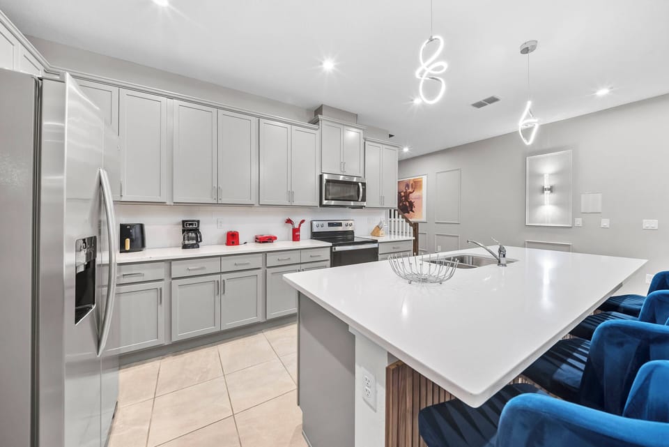 Welcome to a modern kitchen with sleek gray cabinetry and a spacious island topped with polished white countertops. Enjoy the cozy atmosphere created by stylish pendant lights and stainless steel appliances, while relaxing on.