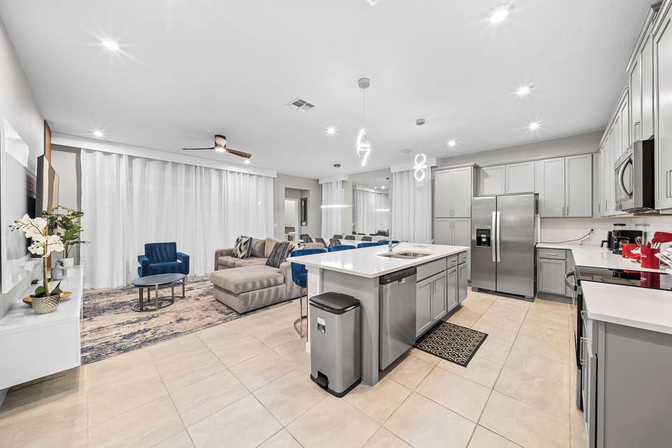 This spacious kitchen flows into a cozy living area, featuring a large quartz island and sleek cabinetry. Soft natural light enhances the modern decor, creating an inviting atmosphere for meals and relaxation together.