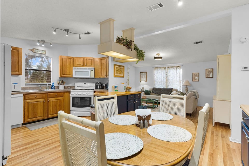 Picture yourself cooking and gathering here—sun-filled open layout blends a fully equipped kitchen with a cozy living space, all bathed in natural light from vaulted ceilings. Your home away from home.