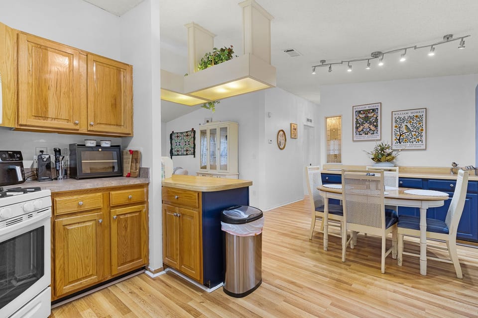 A bright open kitchen and dining area with warm oak cabinetry, track lighting, and space to gather around the table—perfect for cooking meals and connecting over breakfast or dinner.