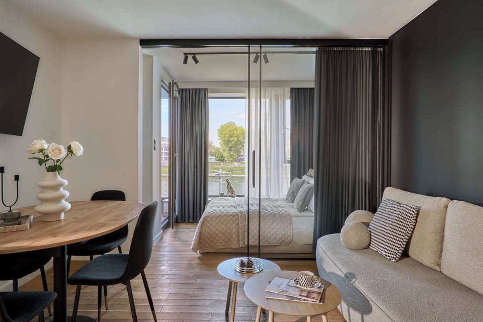 Salon urządzony w nowoczesnym stylu stanowi serce apartamentu. Znajduje się tu wygodna, rozkładana sofa, idealna zarówno do wypoczynku, jak i nocnego relaksu. Naprzeciwko ustawiono telewizor z kanałami TV oraz funkcją Smart TV.