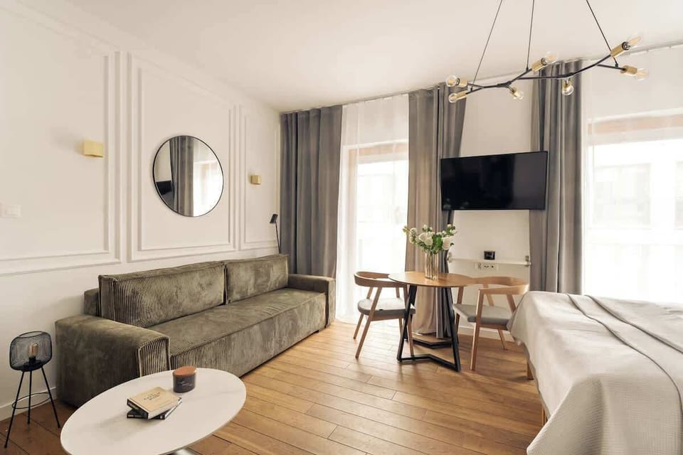 Główna przestrzeń apartamentu łączy strefę wypoczynkową, sypialnianą oraz jadalnianą. Znajduje się tu wygodne łóżko małżeńskie, sprzyjające pełnemu relaksowi po dniu zwiedzania lub pracy, a także komfortowa rozkładana sofa.