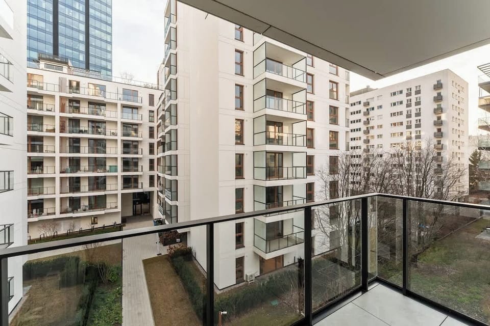 Z salonu prowadzi wyjście na balkon, z którego roztacza się widok na nowoczesne osiedle.