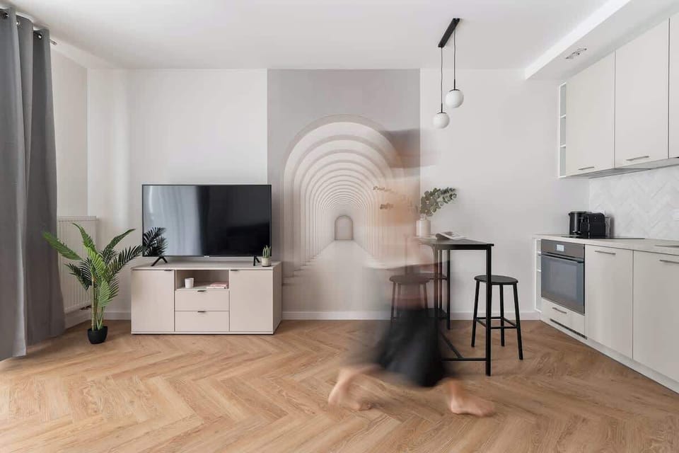 Salon wyposażono w wygodną, rozkładaną sofę, utrzymaną w stonowanych, nowoczesnych odcieniach szarości. Naprzeciwko znajduje się duży telewizor Smart TV z dostępem do kanałów telewizyjnych.