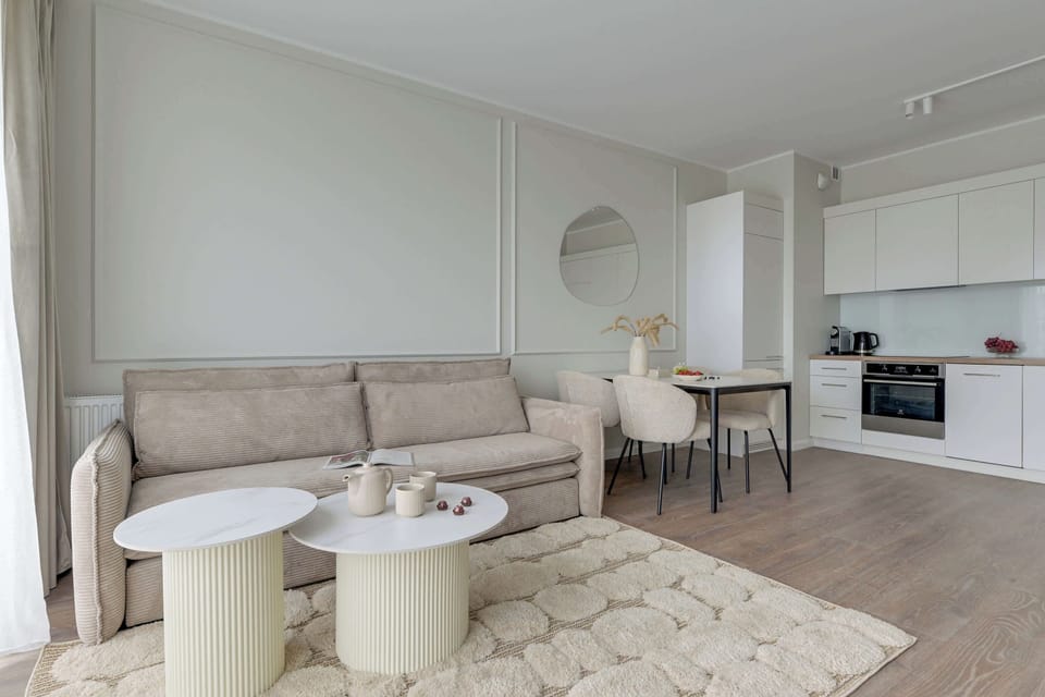 Jasny salon z wygodną sofą i Smart TV zapewnia idealne warunki do relaksu. Klimatyzacja gwarantuje komfort przez cały rok, a duże okna i eleganckie dodatki tworzą przytulną, nowoczesną przestrzeń.