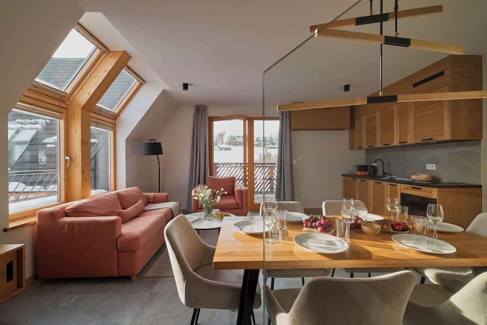 Salon urządzony jest w jasnym, nowoczesnym stylu i stanowi komfortowe miejsce do wspólnego spędzania czasu. Rozkładana sofa, wygodny fotel oraz telewizor sprzyjają relaksowi, a bezpośrednie wyjście na balkon pozwala cieszyć się widokiem na góry.