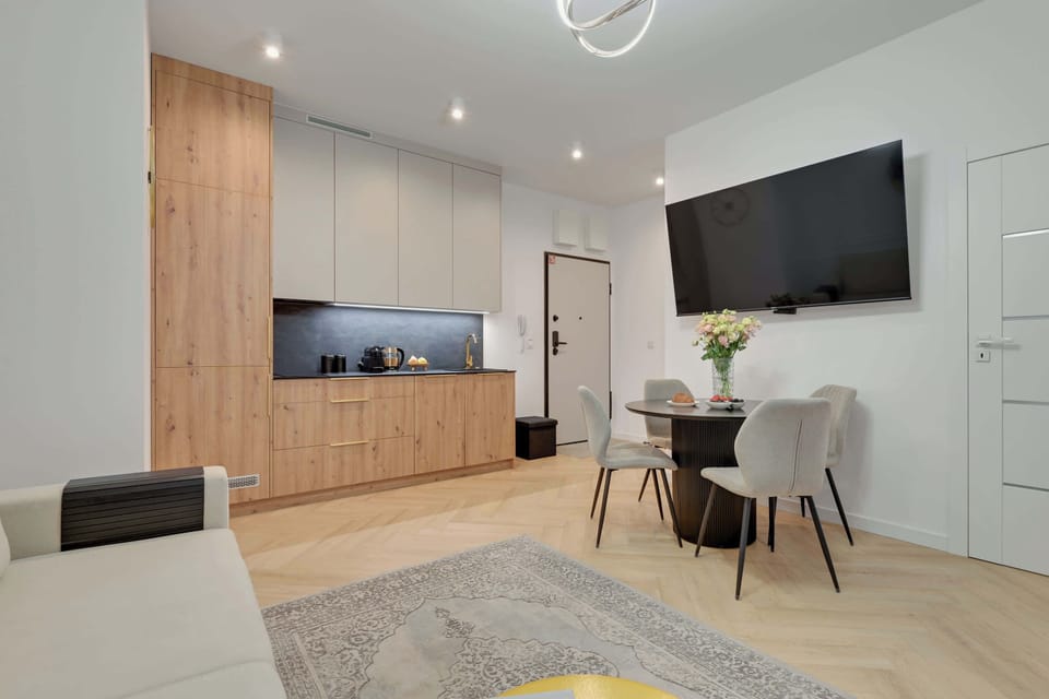 Elegancki salon z aneksem kuchennym zachwyca jasnym, nowoczesnym wystrojem i przytulną atmosferą. Stylowe detale, wygodna sofa oraz funkcjonalna przestrzeń tworzą idealne miejsce do relaksu i wspólnych posiłków.