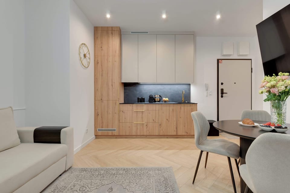Elegancki salon z aneksem kuchennym zachwyca jasnym, nowoczesnym wystrojem i przytulną atmosferą. Stylowe detale, wygodna sofa oraz funkcjonalna przestrzeń tworzą idealne miejsce do relaksu i wspólnych posiłków.