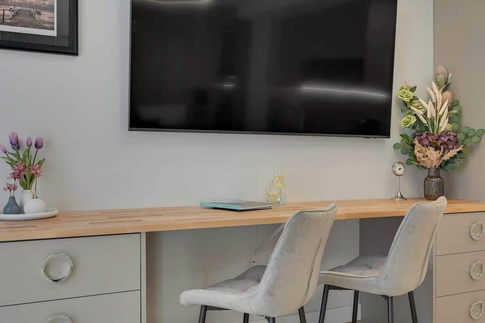 Otwarta przestrzeń z łóżkiem małżeńskim, Smart TV i miejscem do pracy. Wnętrze uzupełniają eleganckie detale, nastrojowe oświetlenie oraz pojemne szafy w przedpokoju.