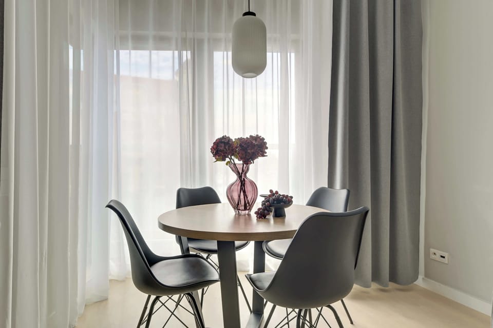 Przestronny salon z aneksem kuchennym w eleganckich, szarych tonacjach zapewnia komfortowy wypoczynek. Duże przeszklenia, wygodna sofa oraz część jadalniana tworzą jasną i nowoczesną przestrzeń sprzyjającą relaksowi.