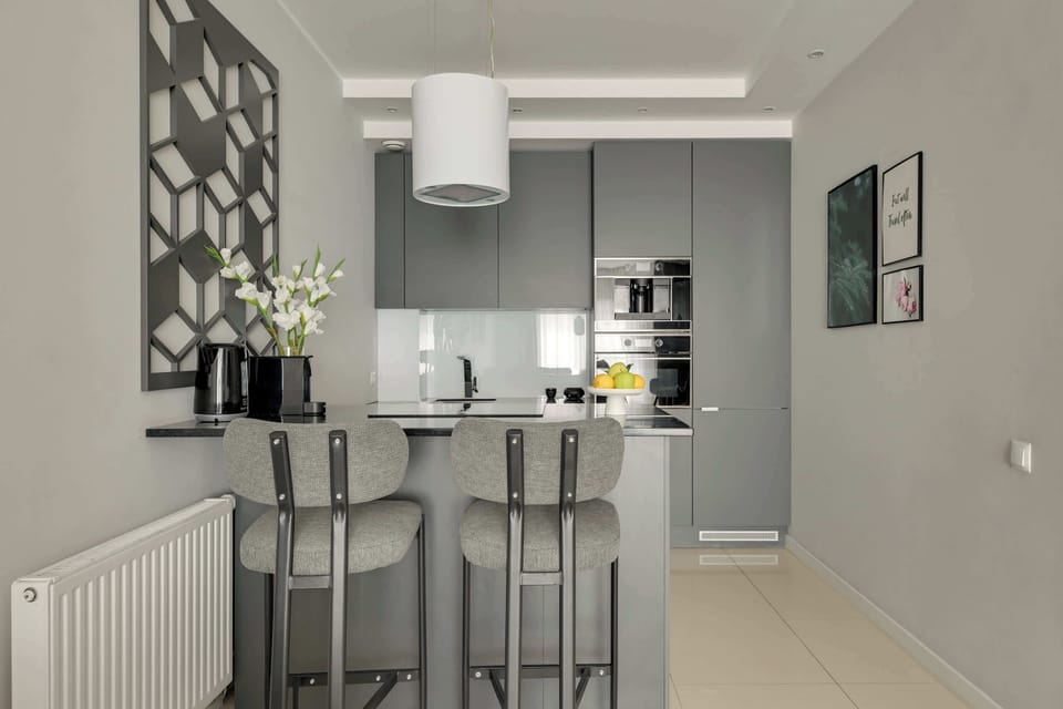 Przestronny salon z aneksem kuchennym w eleganckich, szarych tonacjach zapewnia komfortowy wypoczynek. Duże przeszklenia, wygodna sofa oraz część jadalniana tworzą jasną i nowoczesną przestrzeń sprzyjającą relaksowi.