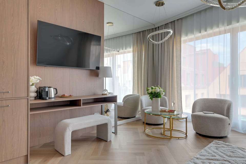 Elegancka część wypoczynkowa z telewizorem, wygodnymi fotelami i dużą zabudową zapewniającą mnóstwo miejsca do przechowywania. Jasne wnętrze, designerskie dodatki i stonowana kolorystyka tworzą atmosferę komfortu i relaksu.