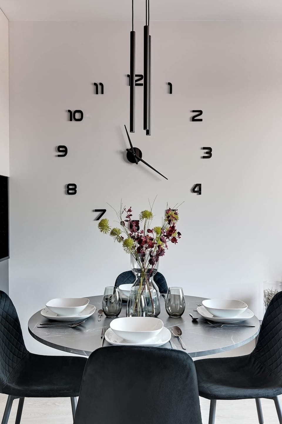 Nowoczesny salon z aneksem kuchennym urządzony w jasnych barwach. Turkusowa sofa, stolik kawowy i miękki dywan tworzą strefę relaksu. Obok znajduje się jadalnia oraz minimalistyczna kuchnia, a duże okno dobrze doświetla wnętrze.
