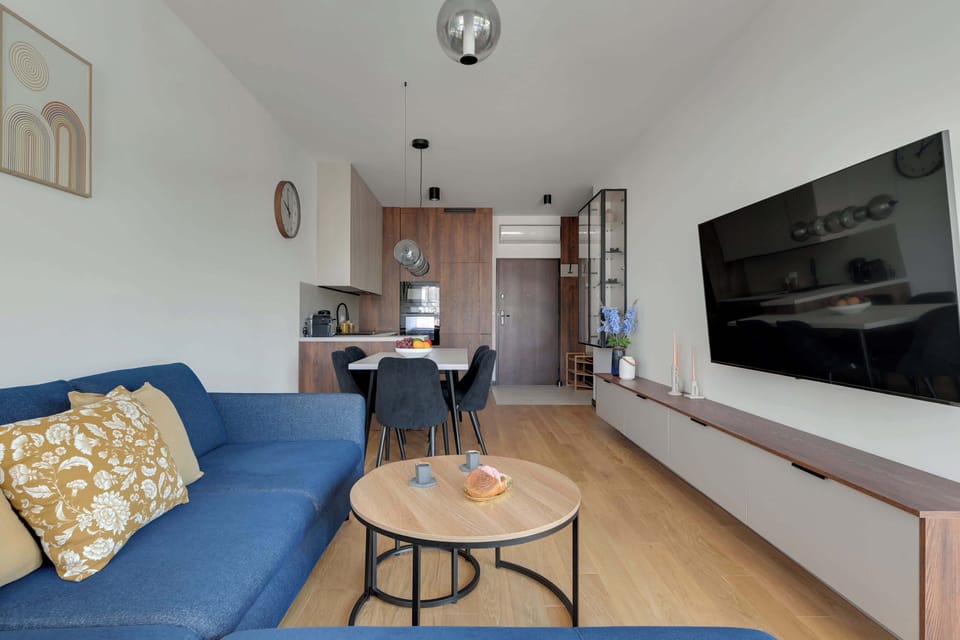 Nowoczesny salon z dużymi przeszkleniami zachwyca jasnym wnętrzem, designerskim oświetleniem i eleganckim wykończeniem. Komfortowa strefa wypoczynku połączona z aneksem kuchennym tworzy idealną przestrzeń do relaksu i wspólnego spędzania czasu.