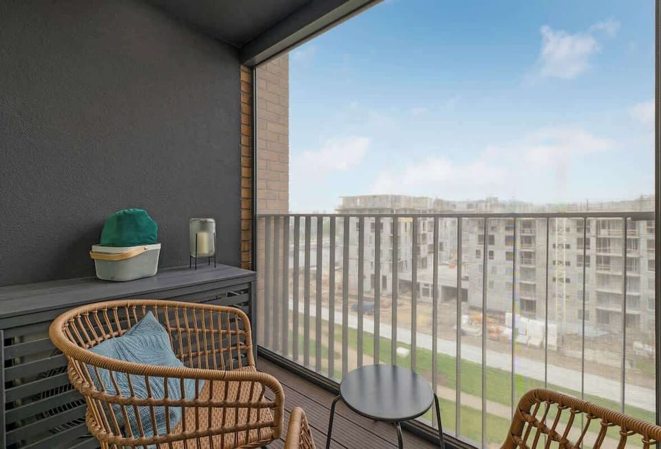 Przestronny balkon z wygodnymi fotelami i stolikiem, idealny na poranną kawę lub chwilę relaksu. Z balkonu rozciąga się widok na nowoczesną zabudowę osiedla.
