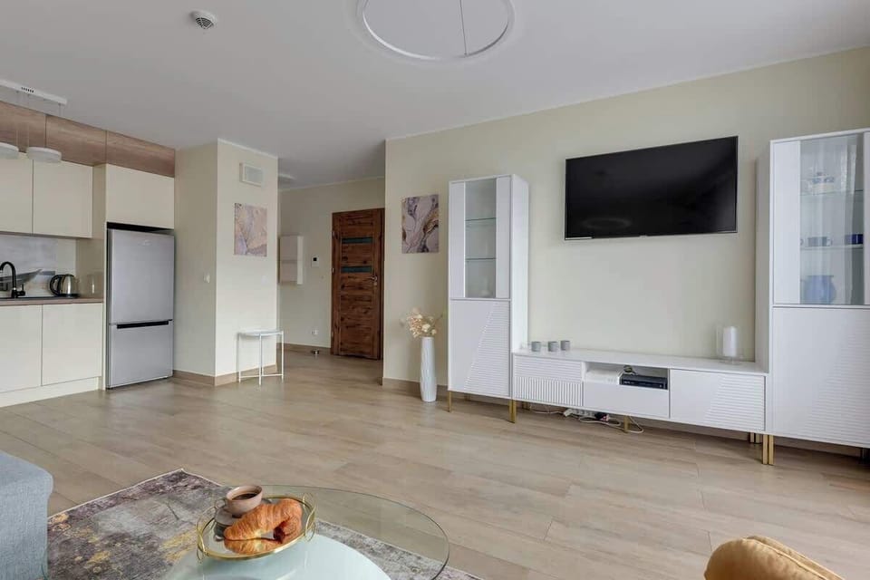 W salonie znajduje się rozkładana sofa zapewniająca dodatkowe spanie, a jasne wnętrze z designerskimi akcentami i dużymi oknami tworzy przytulny, nowoczesny klimat.