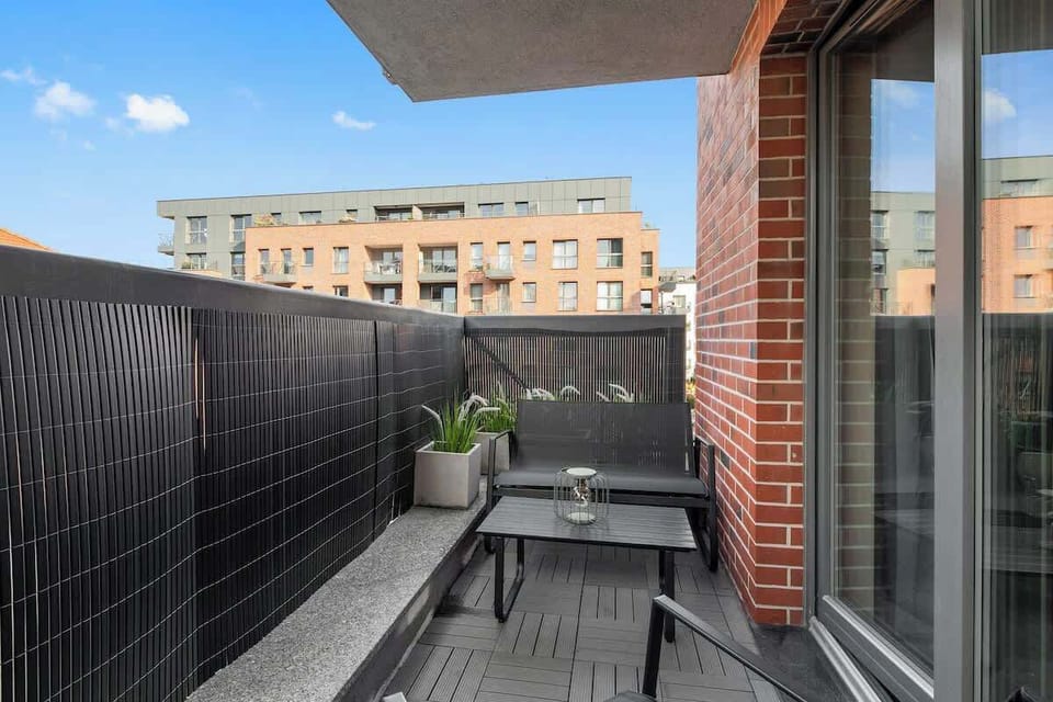 Z salonu prowadzi wyjście na przestronny balkon z meblami ogrodowymi – idealne miejsce na poranną kawę lub wieczorny relaks. Balkon ozdobiony jest girlandami świetlnymi i zielenią, co tworzy kameralną atmosferę.
