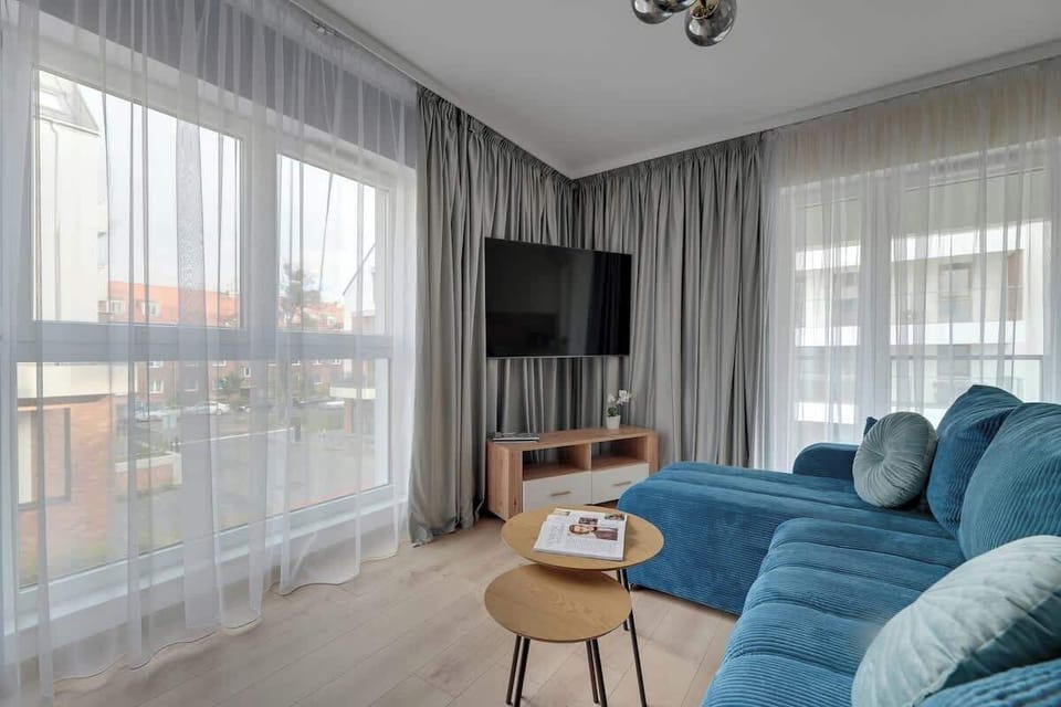 W klimatyzowanym salonie znajduje się duża, rozkładana sofa, telewizor z dostępem do kanałów kablowych oraz funkcją Smart TV. Przestrzeń uzupełnia stół z krzesłami, przy którym można wygodnie zjeść posiłek lub spędzić czas przy wspólnych rozmowach.
