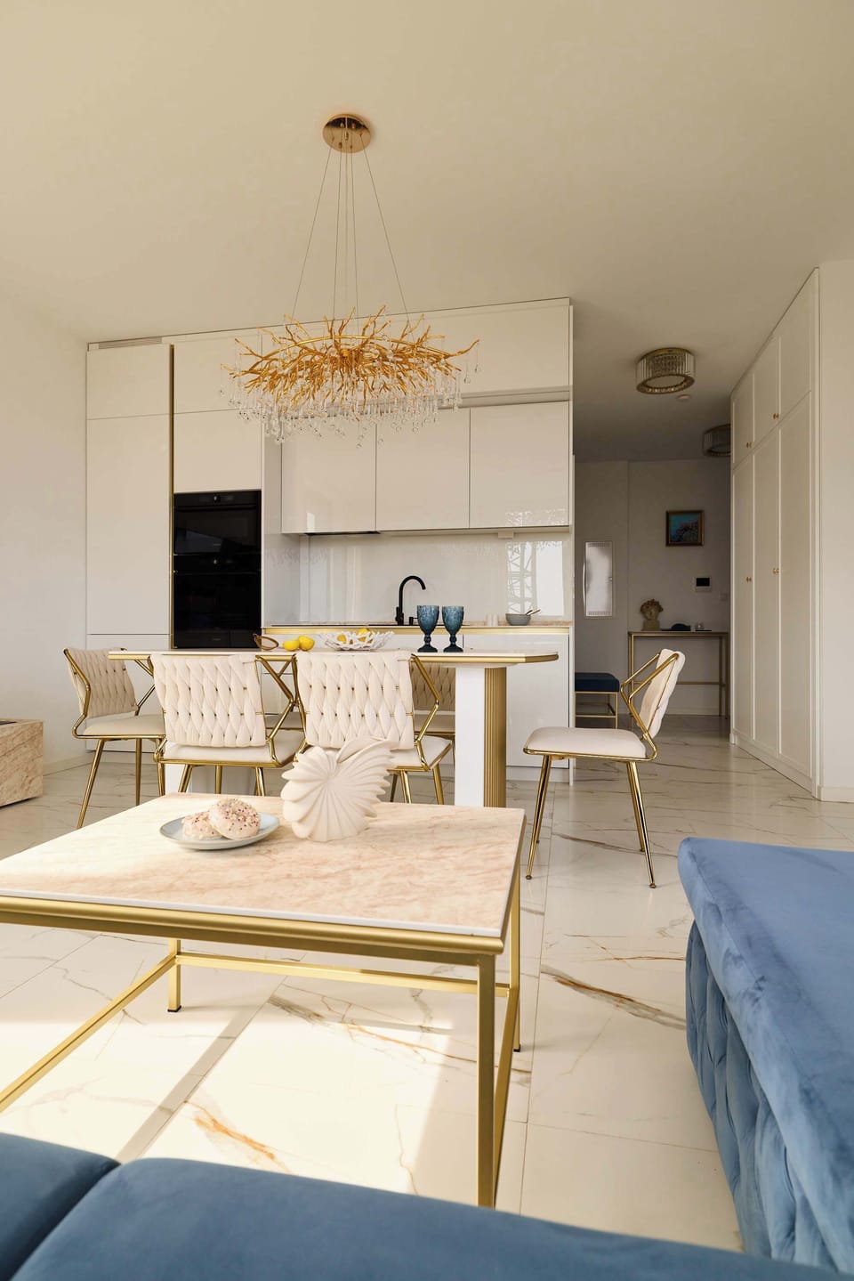 Przestronny salon utrzymany jest w eleganckim, jasnym stylu glamour. Centralnym punktem pomieszczenia jest duża, granatowa sofa z możliwością rozłożenia, idealna do wypoczynku lub jako dodatkowe miejsce do spania.