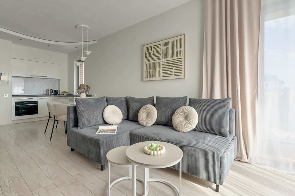 Przestronny salon został urządzony w nowoczesnym, stonowanym stylu. Centralnym elementem części wypoczynkowej jest duża, rozkładana sofa w odcieniu eleganckiej szarości, która zapewnia wygodne miejsce do relaksu.