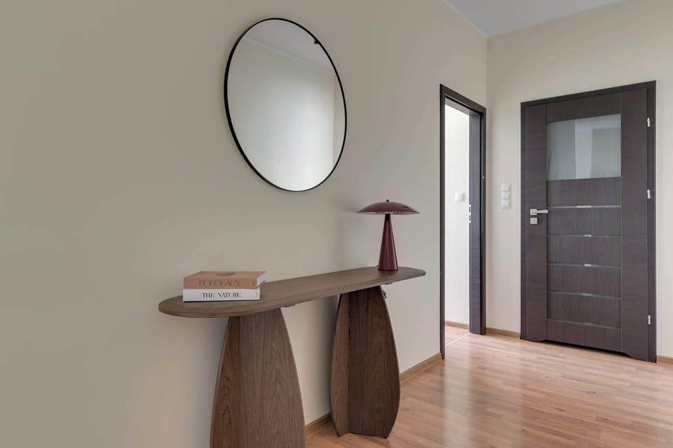 Przestronny salon z częścią jadalnianą, urządzony w eleganckich odcieniach bieli i bordo. Duże przeszklenia zapewniają mnóstwo naturalnego światła, a wygodna sofa i stół dla czterech osób tworzą idealne miejsce do wypoczynku i wspólnych posiłków.