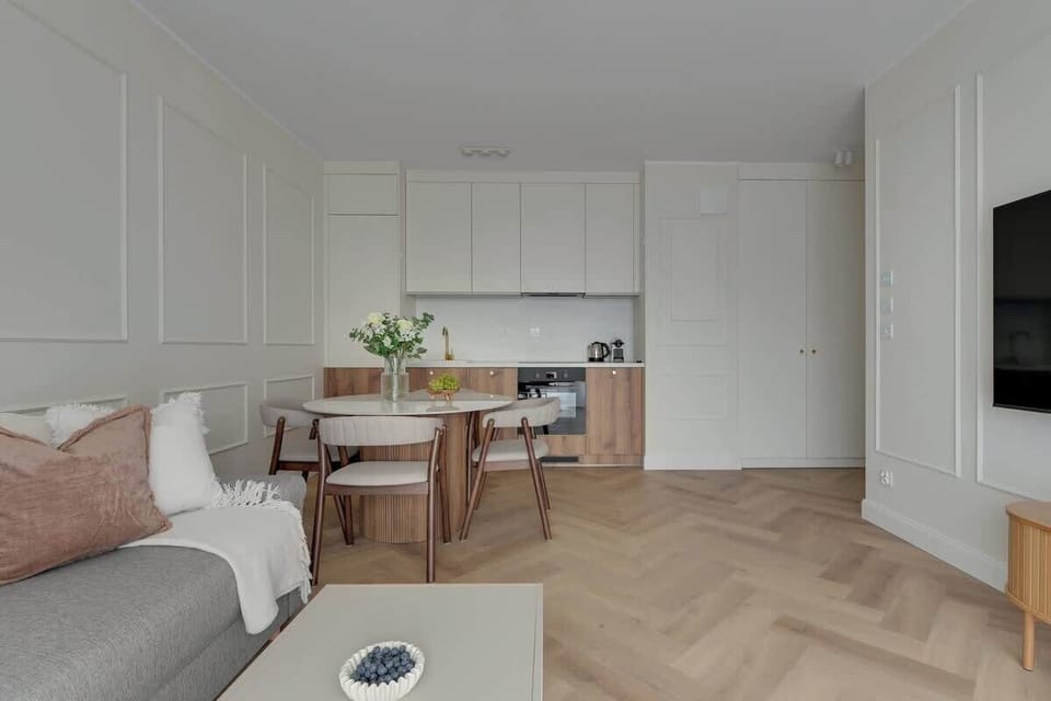 Stylowy salon w jasnych barwach oferuje komfortowy wypoczynek dzięki rozkładanej sofie oraz dużemu telewizorowi z funkcją Smart TV.