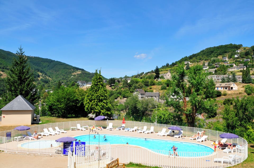  Outdoor heated pool with sun loungers and parasols, set against the rolling green hills of the Aveyron gorges.