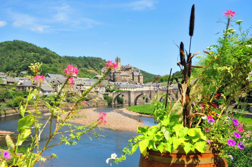 Colourful blooms frame a view of the medieval village of Entraygues-sur-Truyères and its iconic stone bridge over the Lot river.