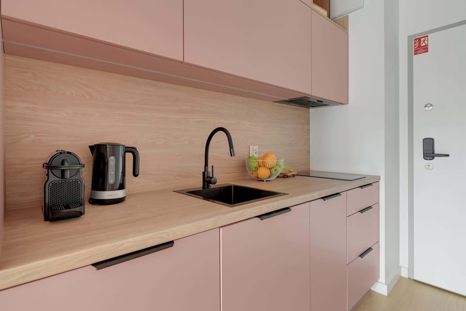 Stylowy aneks kuchenny w pudrowych odcieniach łączy nowoczesny design z funkcjonalnością. Jasne drewniane akcenty, pełne wyposażenie oraz minimalistyczne detale tworzą przytulną i elegancką przestrzeń.