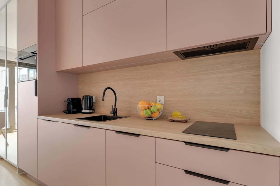 Stylowy aneks kuchenny w pudrowych odcieniach łączy nowoczesny design z funkcjonalnością. Jasne drewniane akcenty, pełne wyposażenie oraz minimalistyczne detale tworzą przytulną i elegancką przestrzeń.