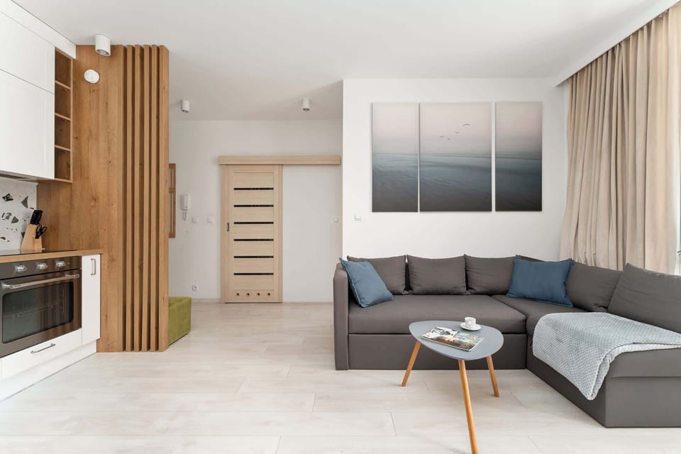 Centralną częścią apartamentu jest salon z rozkładaną sofą, telewizorem z kanałami kablowymi i funkcją Smart TV oraz wyjściem na balkon. Duże przeszklenia zapewniają wnętrzu dużo naturalnego światła.