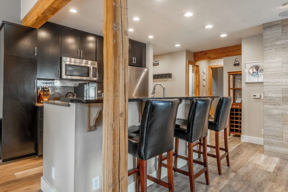 Gather at your modern breakfast bar beneath warm wood beams, where stainless appliances and sleek cabinetry make meal prep a breeze in this open, inviting kitchen space.