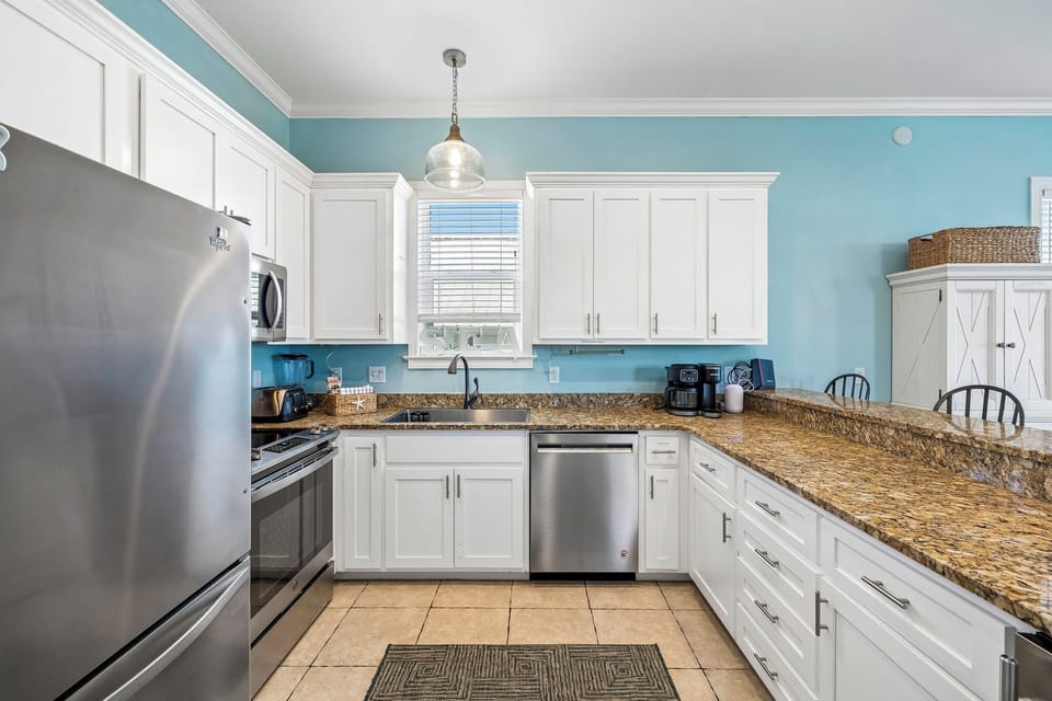 Step into your bright, fully-equipped kitchen where coastal blue walls and granite countertops create the perfect backdrop for your morning coffee or family meals together.