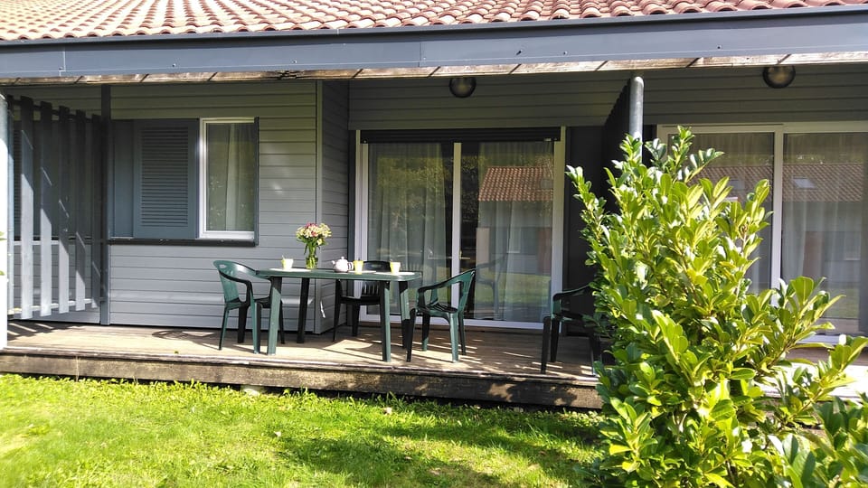 Covered terrace with a dining table and garden chairs, steps from the lake.