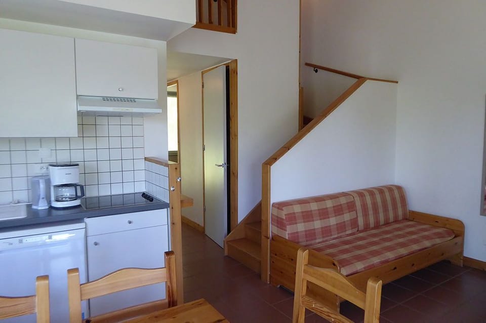The open living area with kitchenette, dining table, sofa beds, and stairs to the upper floor.