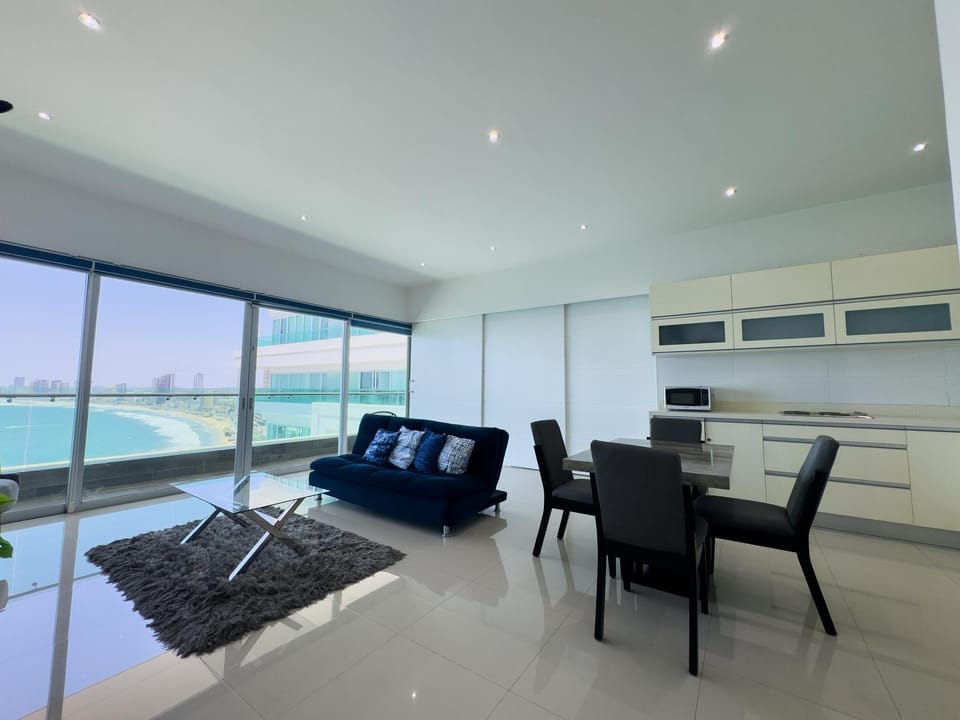 Living room with navy sofa, glass coffee table on gray shag rug, and sliding doors revealing ocean views.