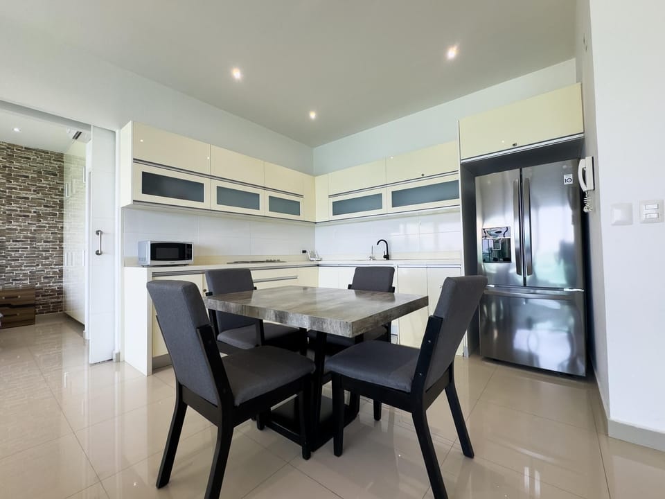 Square dining table with concrete top surrounded by four gray cushioned chairs in the kitchen area.