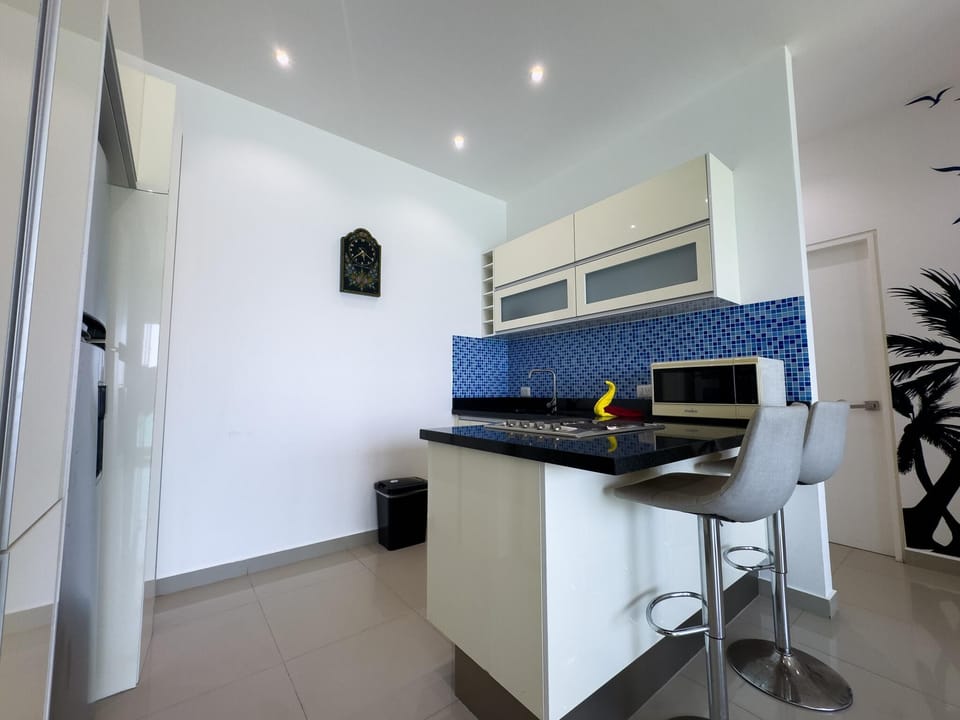 Black granite countertop island with two gray bar stools, blue mosaic tile backsplash, and white cabinetry.