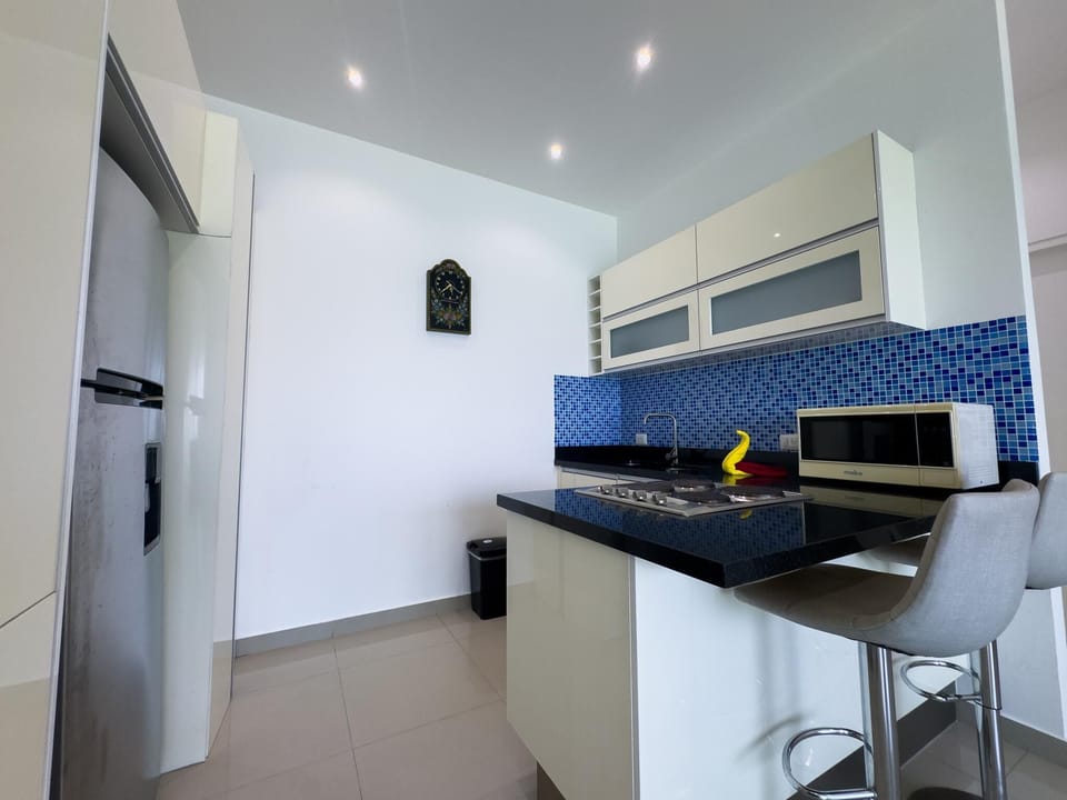 Black granite island with built-in stove and two gray barstools faces blue mosaic tile backsplash in the kitchen.