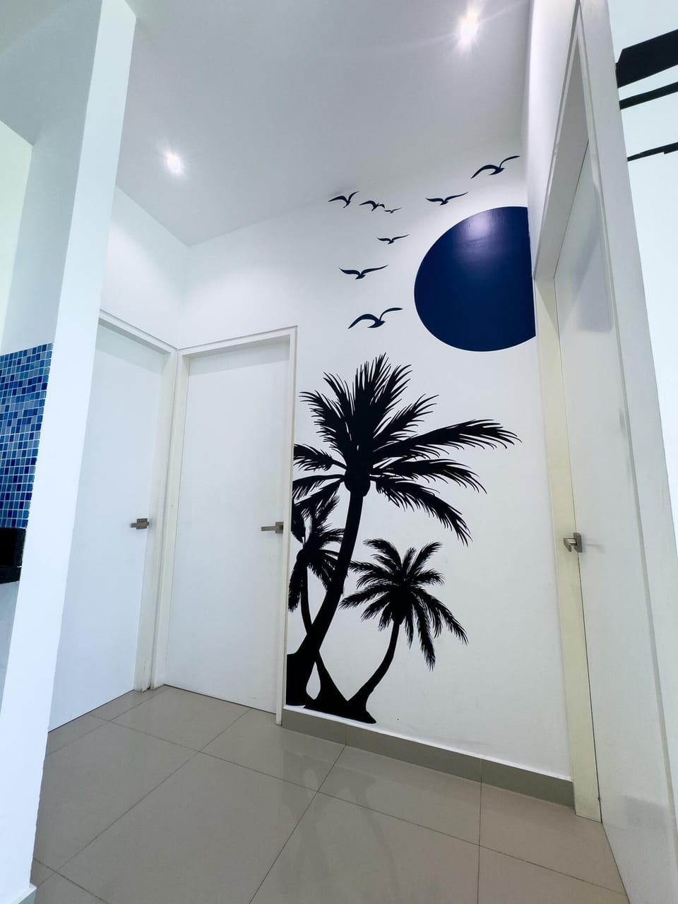 Hallway corner featuring white doors, glossy beige tile floor, and a black palm tree mural with flying birds and a dark blue sun.