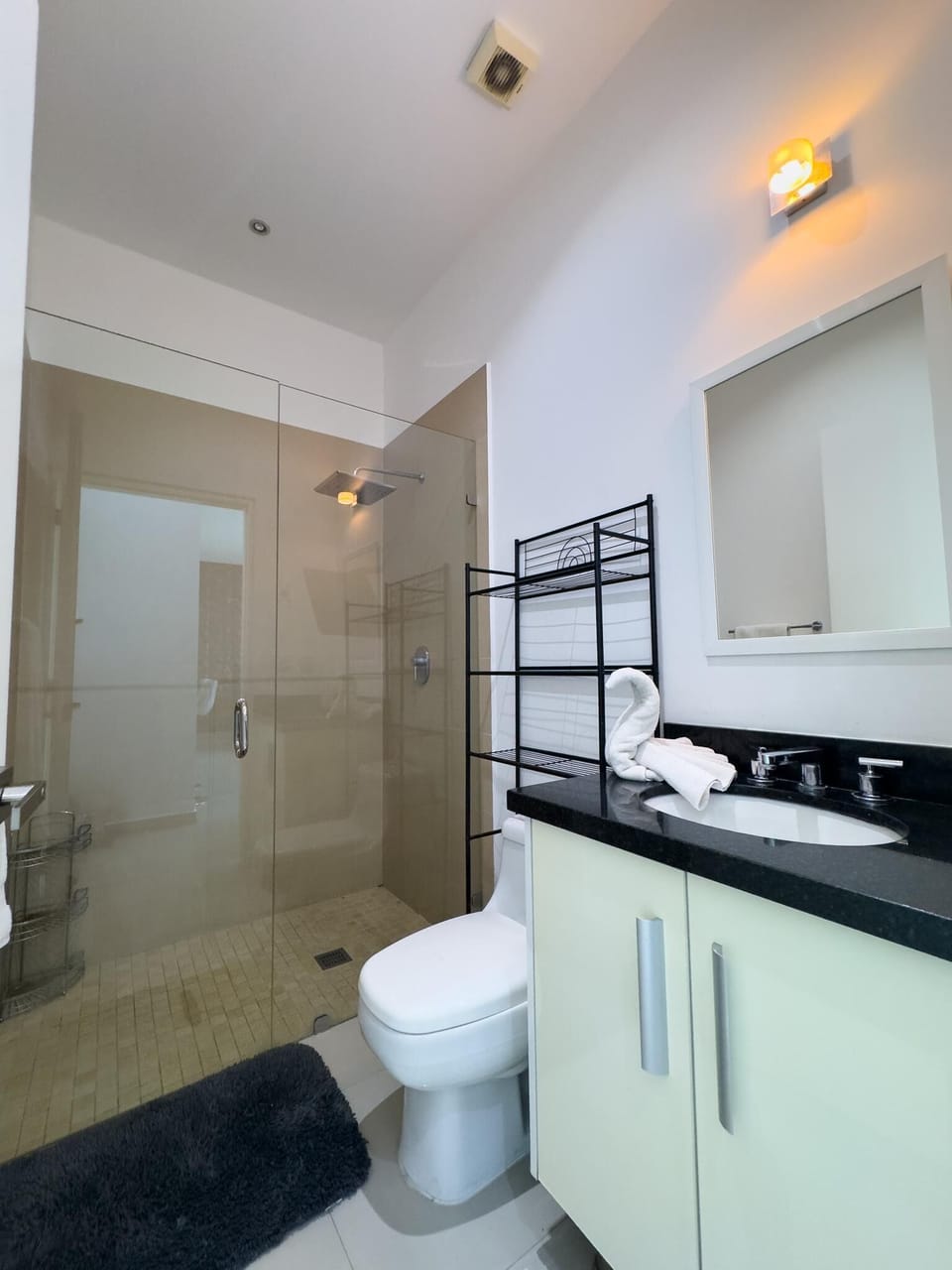 Glass-enclosed shower with beige tile walls, black granite countertop, and white vanity in the bathroom.