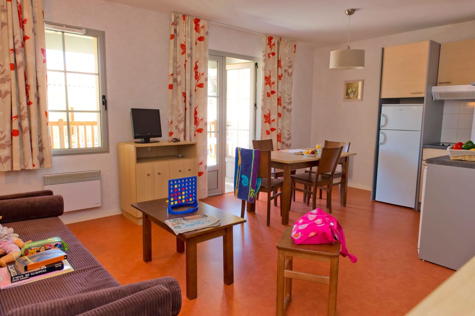 Balcony doors open onto the terrace, with the dining table, sofa bed, TV, and kitchen corner all in one space.