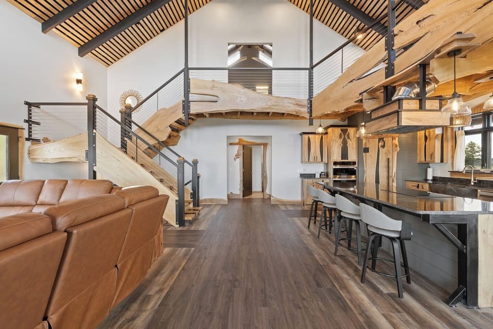 Open-concept living space featuring a seamless flow between the living area and kitchen, highlighted by high vaulted ceilings, warm wood accents, and a staircase leading to an upper loft level.