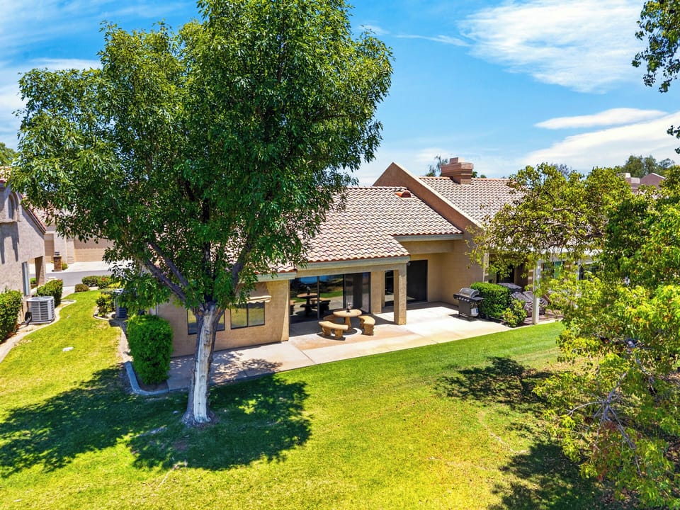 Aerial view of the home's rear exterior, emphasizing the deep shaded patio and lush lawn spaces