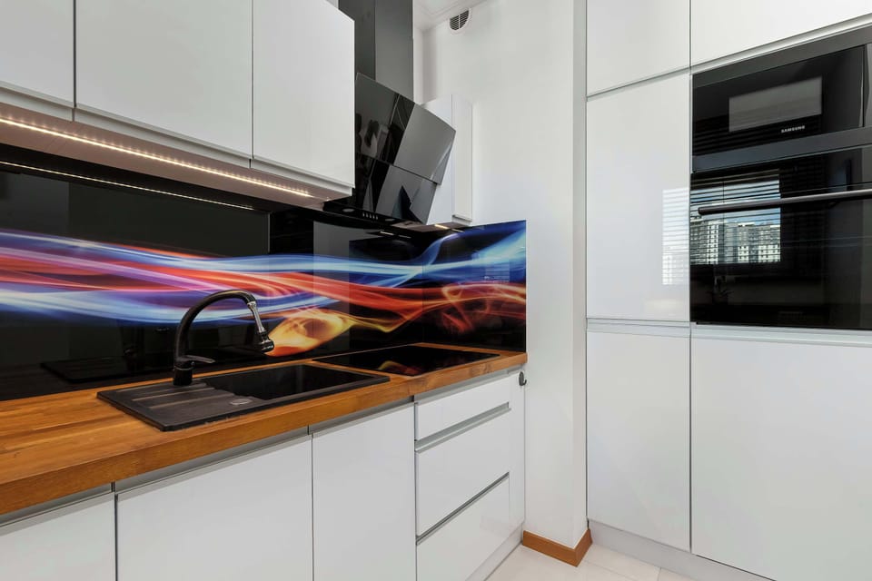 A detailed view of the kitchen workspace highlights the built-in black sink, matching faucet, and an integrated oven. The vibrant, illuminated glass panel backsplash creates a strong modern focal point.