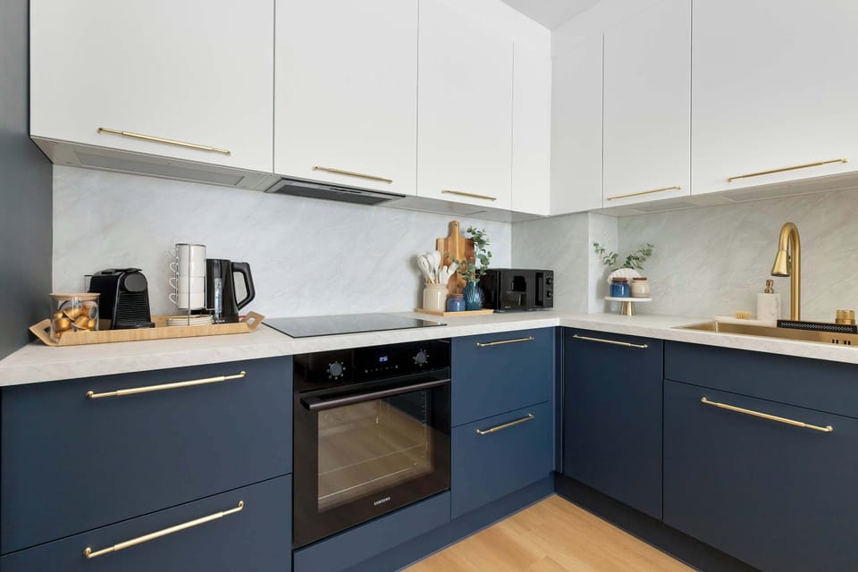 Another angle of the modern kitchen highlights the clean white countertops and navy cabinetry. Essential kitchen appliances and cooking accessories are neatly arranged on the surface.