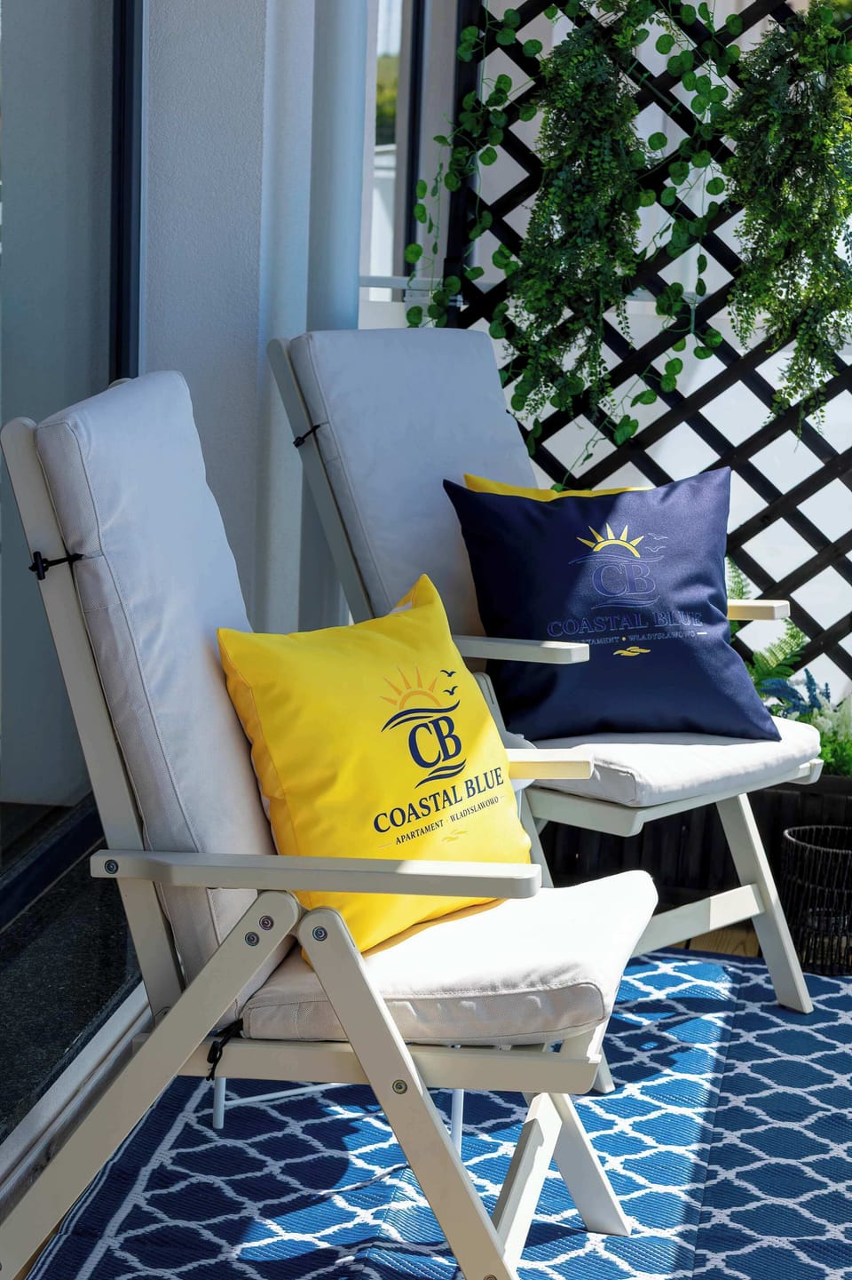 A vertical perspective of the balcony area showcases two outdoor chairs with comfortable cushions. A patterned blue outdoor rug lies beneath the seating arrangement to complete the cozy setup.
