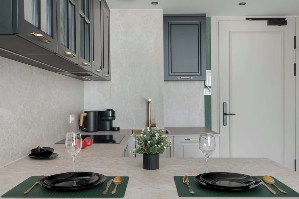 A close-up view over the kitchen counter shows two black plates and gold cutlery set for a meal. A small plant adds a welcoming touch.