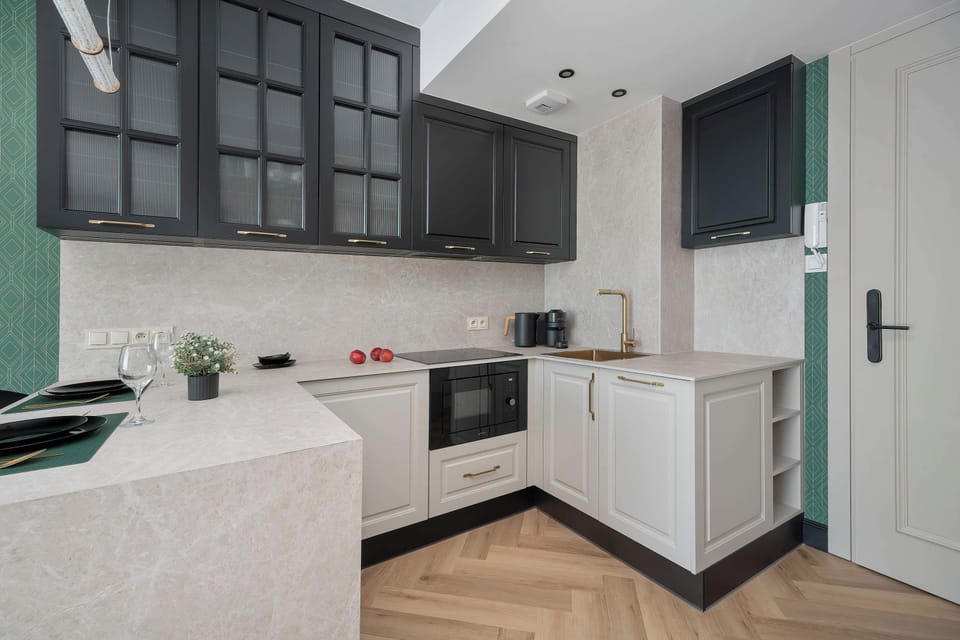 The L-shaped kitchen features off-white cabinetry, dark glass upper cabinets, and a light counter. A microwave and hob are neatly integrated.